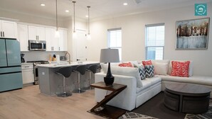 A modern kitchen with a central island, bar stools, a white sofa with patterned cushions, and a dining area with a round table. - R3 at Inlet Beach with Pool access and EV charger (Inlet Beach)