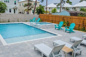 A swimming pool with a wooden deck, surrounded by turquoise Adirondack chairs and white lounge chairs.
