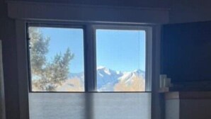 Une pièce dotée d’une grande fenêtre donnant sur les montagnes, d’un canapé de couleur sombre et d’une petite table sur laquelle repose un livre.