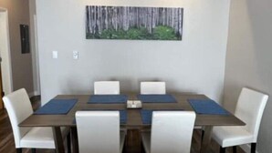 Un coin repas avec une table rectangulaire, six chaises blanches et des sets de table bleus.