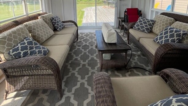 Un patio couvert aménagé avec des meubles en osier, une table centrale et une chaise rouge.