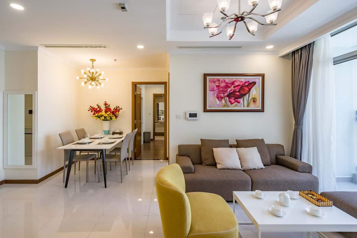 Uma sala de estar moderna com um sofá, uma mesa de jantar posta para quatro pessoas, uma poltrona amarela e uma mesa de centro com xícaras de chá.