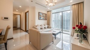 A modern living room with a sofa, a dining table, and a large window with a city view. - Vinhomes Central Park Riverside Elegance (Ho Chi Minh City)