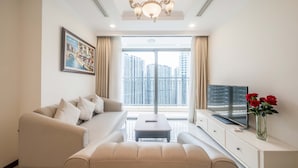 A modern living room with a sofa, a coffee table, a TV, and a vase with flowers. - Vinhomes Central Park Riverside Elegance (Ho Chi Minh City)