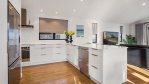 A modern kitchen with white cabinetry, stainless steel appliances, and a wooden floor. - Waterfront Oasis - Omokoroa Holiday Home (Omokoroa)