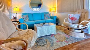 Ein Wohnzimmer mit einem blauen Sofa, einem runden Spiegel, einem Korbtisch und einem gemusterten Teppich.