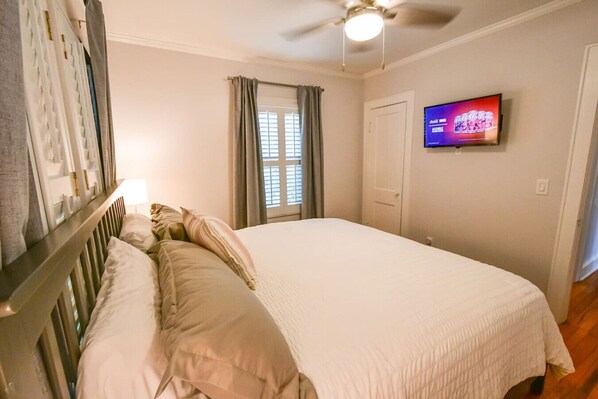Un dormitorio con cama, televisor, ventana con cortinas y ventilador de techo.