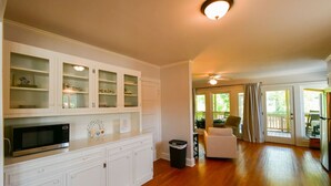 A spacious kitchen with white cabinetry, a microwave, and a trash bin. There is a dining area with a white chair and a table. - Toccoa River House- Toccoa River Front-2br/2ba-wifi-walk to town-Free Activities (McCaysville)