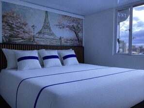 A hotel room with a bed, a painting of the Eiffel Tower, and a window with the 'UNT' sign. - Paramount Hotel (Bogotá)