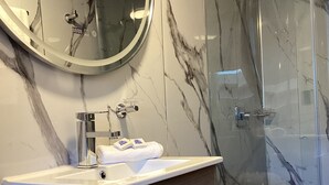 A bathroom with a marble vanity, a toilet, and a glass shower enclosure. - Paramount Hotel (Bogotá)