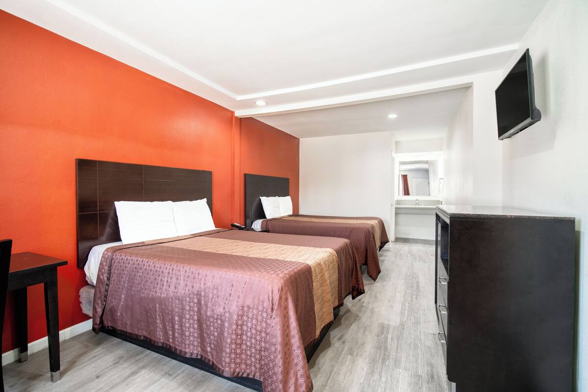A hotel room with two beds, a desk, and a TV.