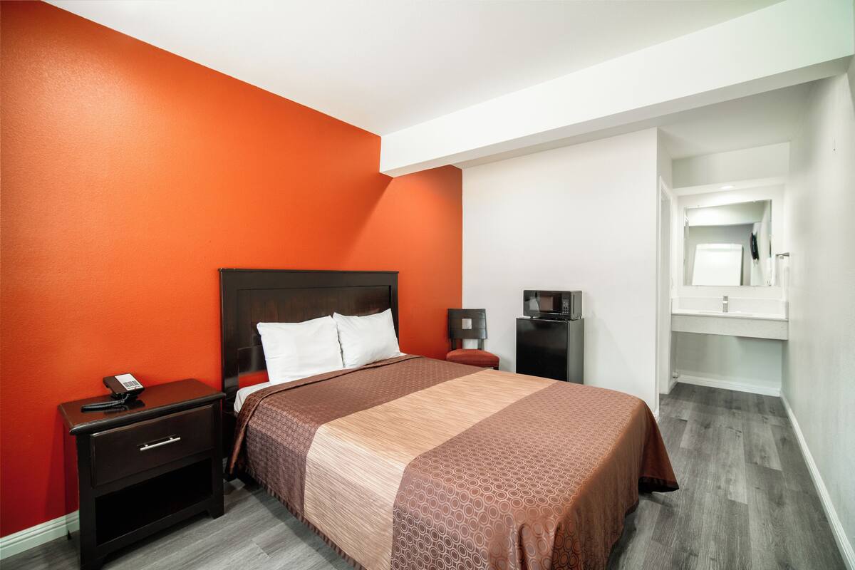 A hotel room with a bed, a nightstand, a desk, and a mirror.