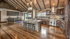 A spacious kitchen with a large island, wooden beams, and stone accents. - Heated pool & hot tub at huge mountain retreat

 (Cherry Log)