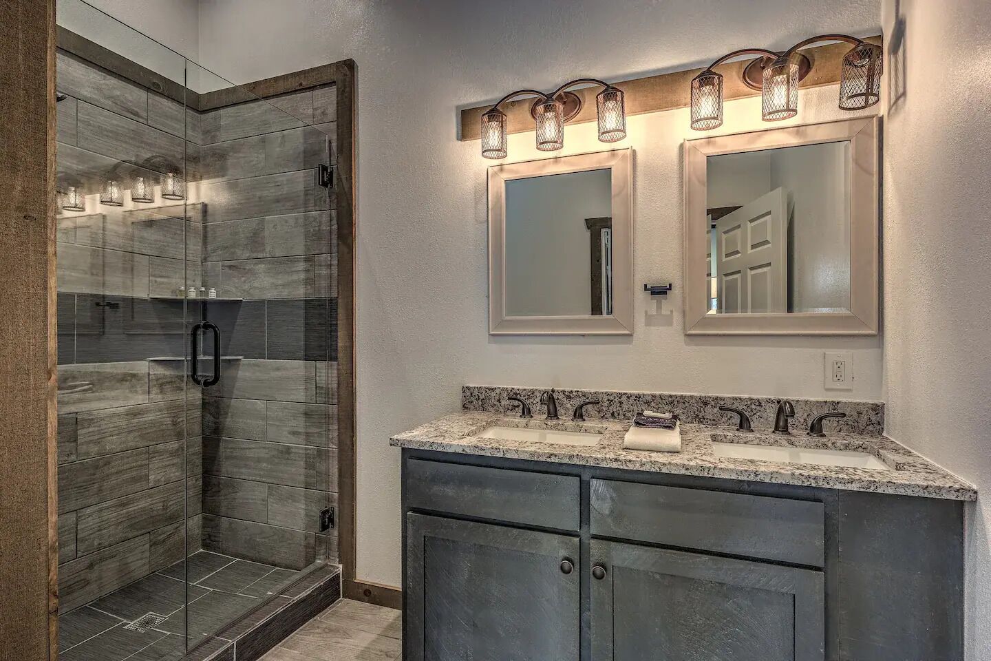A bathroom with a shower, two mirrors, and a granite countertop with a sink.