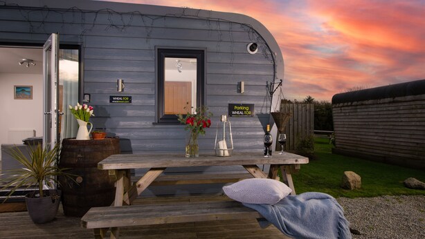 A caravan with a wooden exterior, a picnic table, and a sign indicating a parking area. - Wheal Tor Lodge (Helston)
