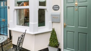 Un coin d’un bâtiment avec une porte bleue, une fenêtre à cadre blanc, une boîte aux lettres et une petite plante en pot.