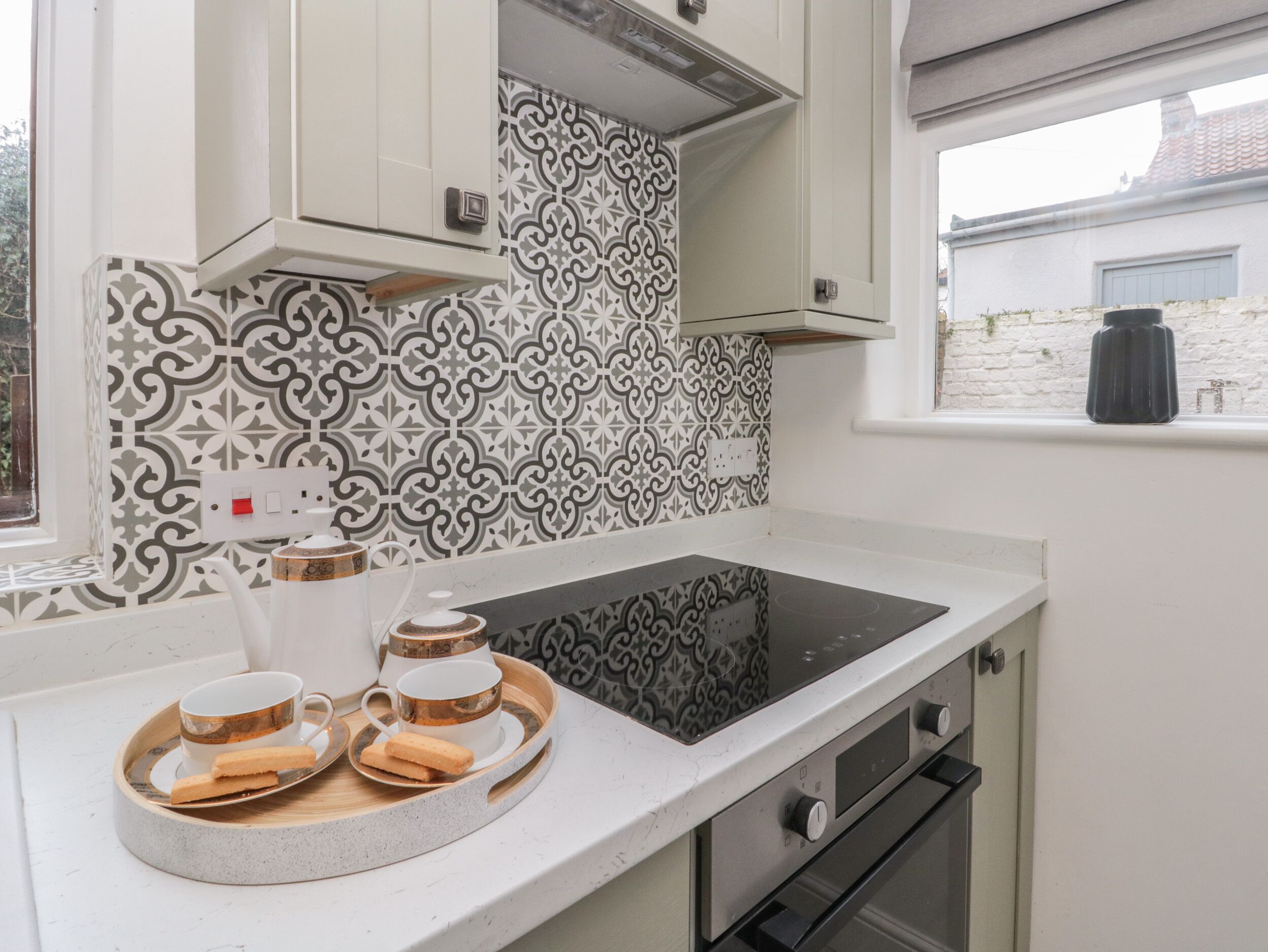 Een moderne keuken met een zwart inductiekookveld, witte kastjes en een decoratieve spatwand.