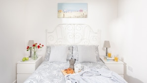 A neatly arranged bedroom with a bed, bedside tables, a lamp, a coffee maker, a plate with food, a cup, and a vase with flowers. - Wheal Jewel Lodge (Helston)