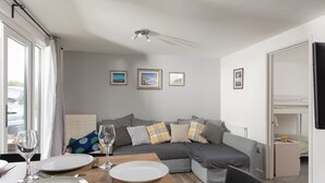 A modern living room with a grey sectional sofa, a dining table set with plates and cutlery, and framed pictures on the wall. - Wheal Jewel Lodge (Helston)