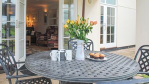 An outdoor patio with a round metal table, chairs, a vase with flowers, and a plate of muffins. - 5 Thurlestone Beach (Kingsbridge)
