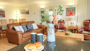 A living room with a brown leather sofa, two patterned mugs, a vase with flowers, and a plate of croissants. - 5 Thurlestone Beach (Kingsbridge)