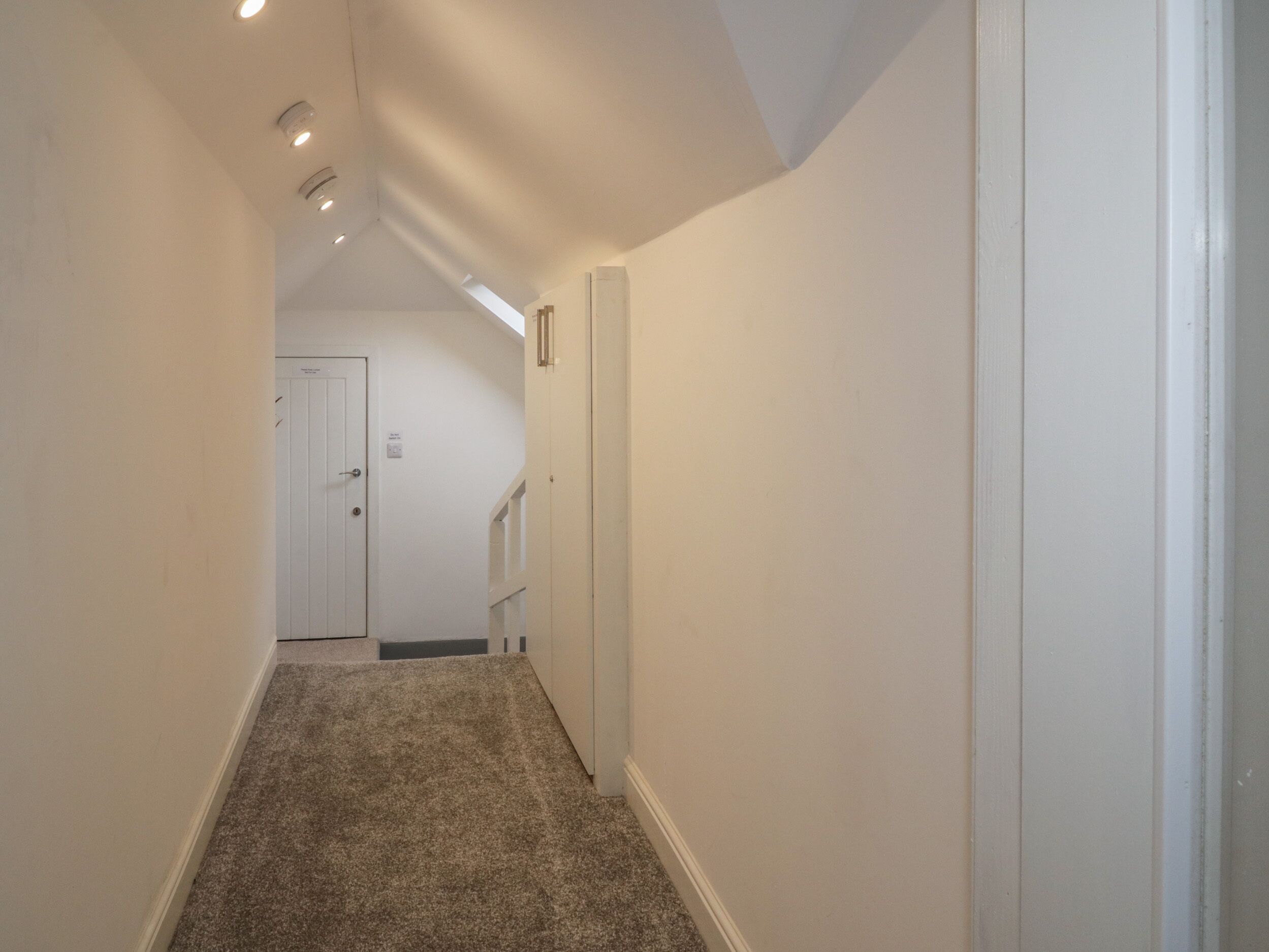A narrow hallway with carpeted floors and white walls.