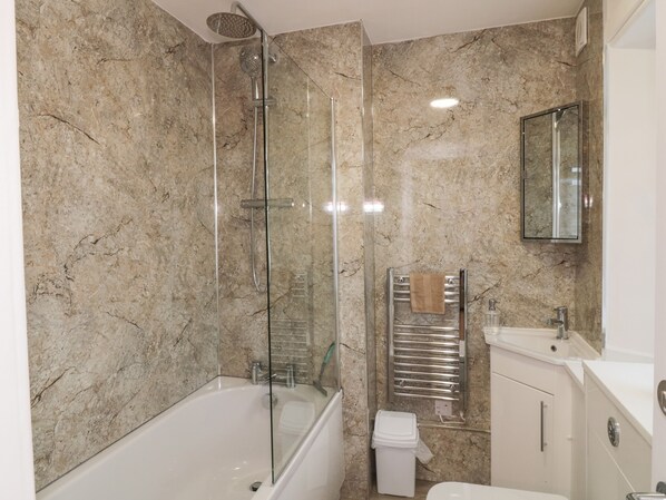 Un baño moderno con ducha envuelta en cristal, bañera blanca y lavamanos integrado.
