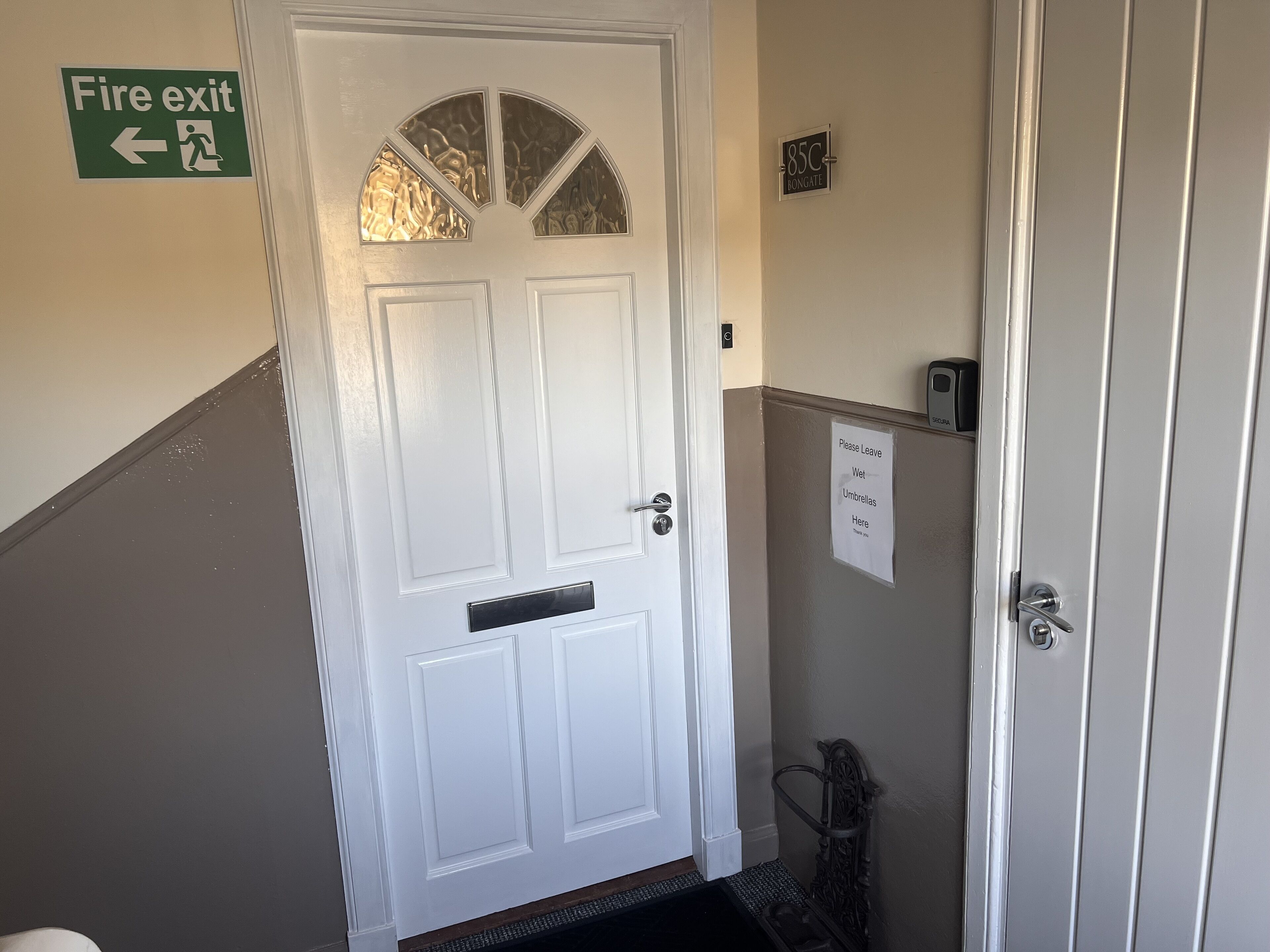 A white door with a fire exit sign above it, a doorbell, and a sign indicating a place to leave wet umbrellas.