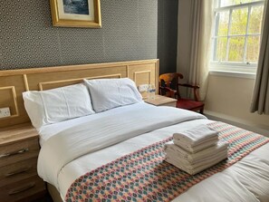 A neatly made bed with white linens, a patterned throw blanket, and a stack of folded towels. - Earl David Hotel (Kirkcaldy)
