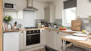 A modern kitchen with white cabinets, a built-in microwave, a gas stove, and a stainless steel range hood. - Bushwood Lodge (Helston)