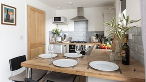A modern kitchen with a wooden dining table set for four, a microwave, a gas stove, and a variety of kitchen utensils. - Bushwood Lodge (Helston)