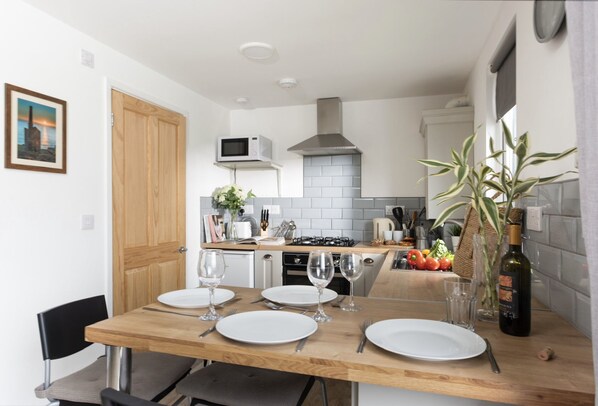Una cocina moderna con una mesa de comedor de madera dispuesta para cuatro personas, un microondas, una estufa a gas y una variedad de utensilios de cocina.