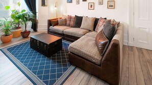 A living room with a sectional sofa, a coffee table, and a chandelier. There are potted plants, a rug, and framed pictures on the walls. - Desswood Aberdeen City Apartment (Aberdeen)