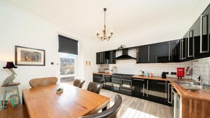 A modern kitchen with black cabinets, a wooden dining table, and a chandelier. - Desswood Aberdeen City Apartment (Aberdeen)