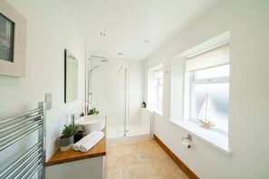 Ein modernes Badezimmer mit Glasdusche, Waschbecken mit Spiegel, Handtuchhalter und einem Fenster mit Segelboot-Dekoration.