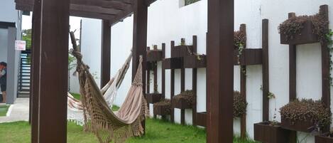 A hammock under a wooden pergola, surrounded by white walls with vertical wooden planters containing plants.