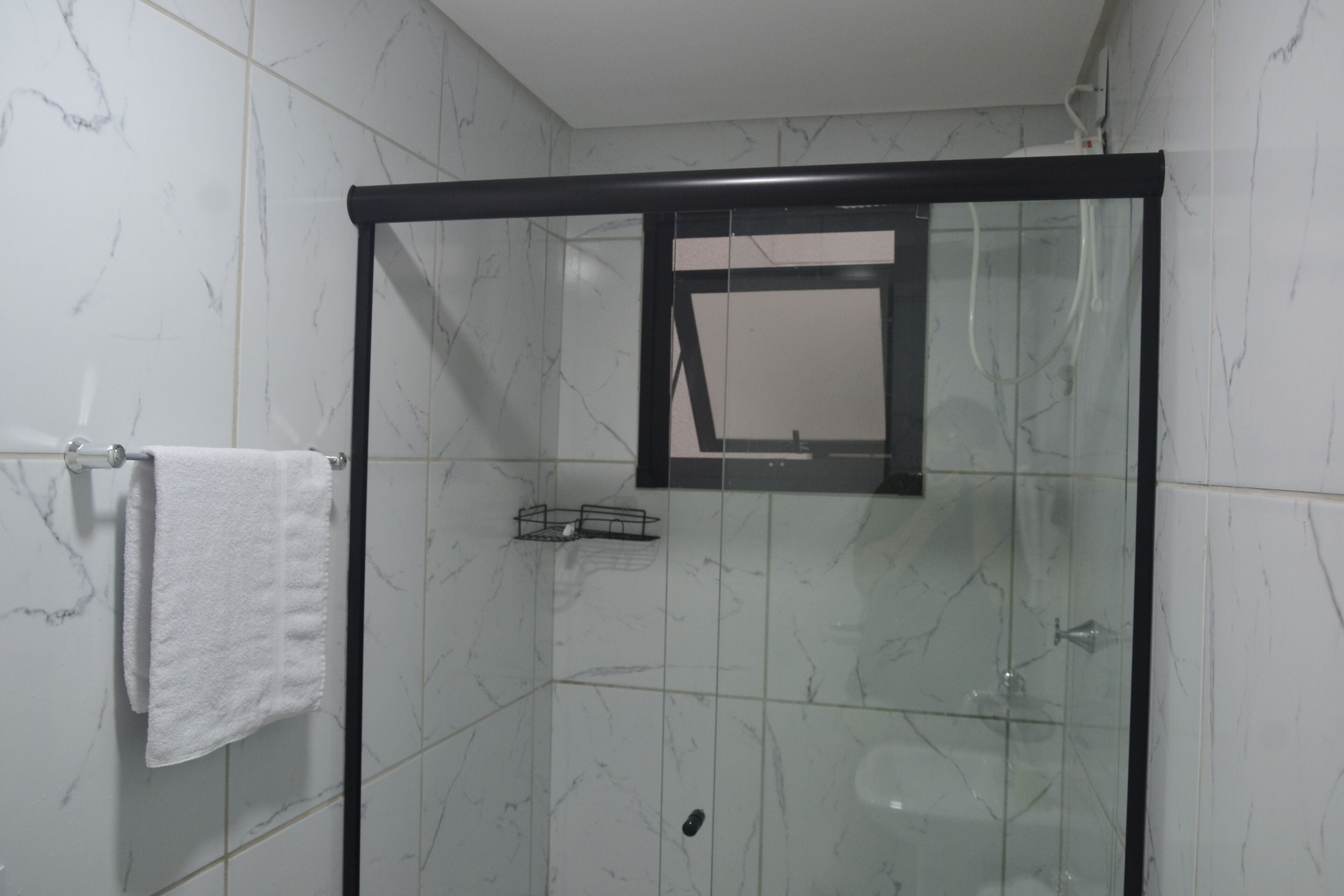 A glass-enclosed shower with a black frame, white marble tiles, and a white towel hanging on a metal rack.