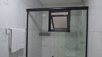 Een douche met glazen wanden, een zwart frame, witte marmeren tegels, en een witte handdoek die hangt aan een metalen rek.