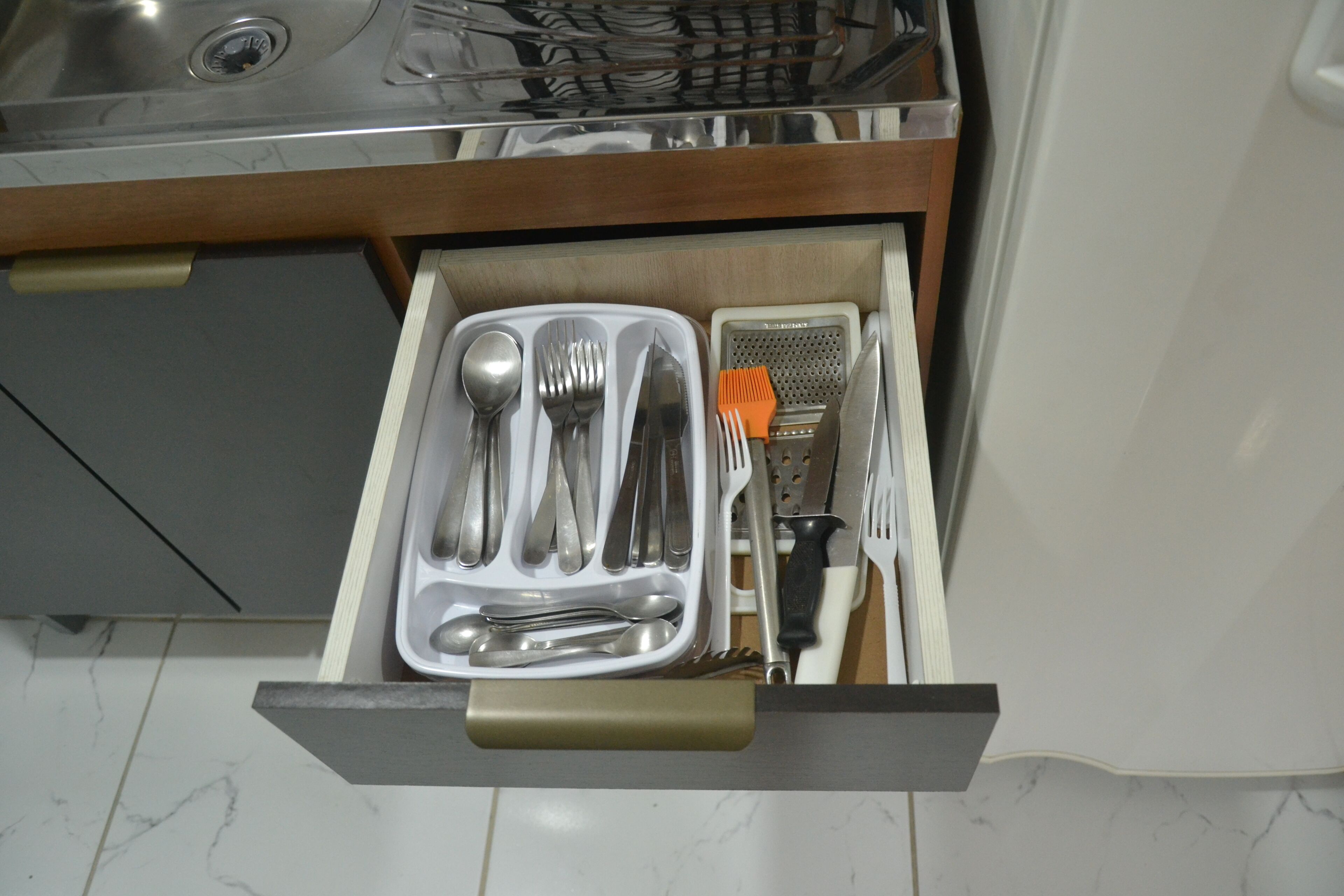 A kitchen drawer with utensils and a grater.