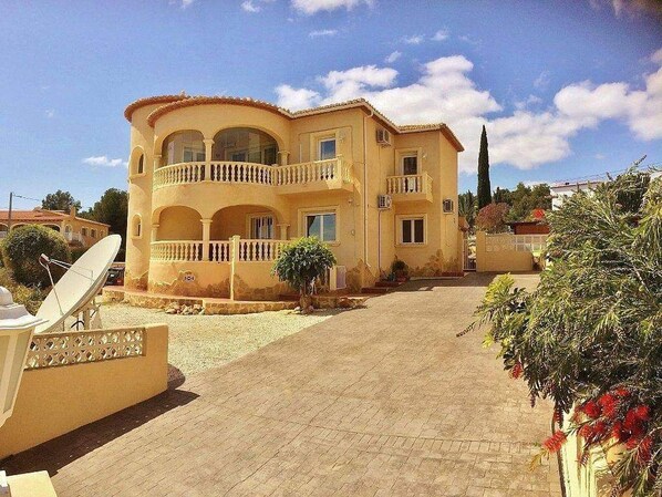 Una casa a due piani con un balcone, un'antenna parabolica e un vialetto lastricato.