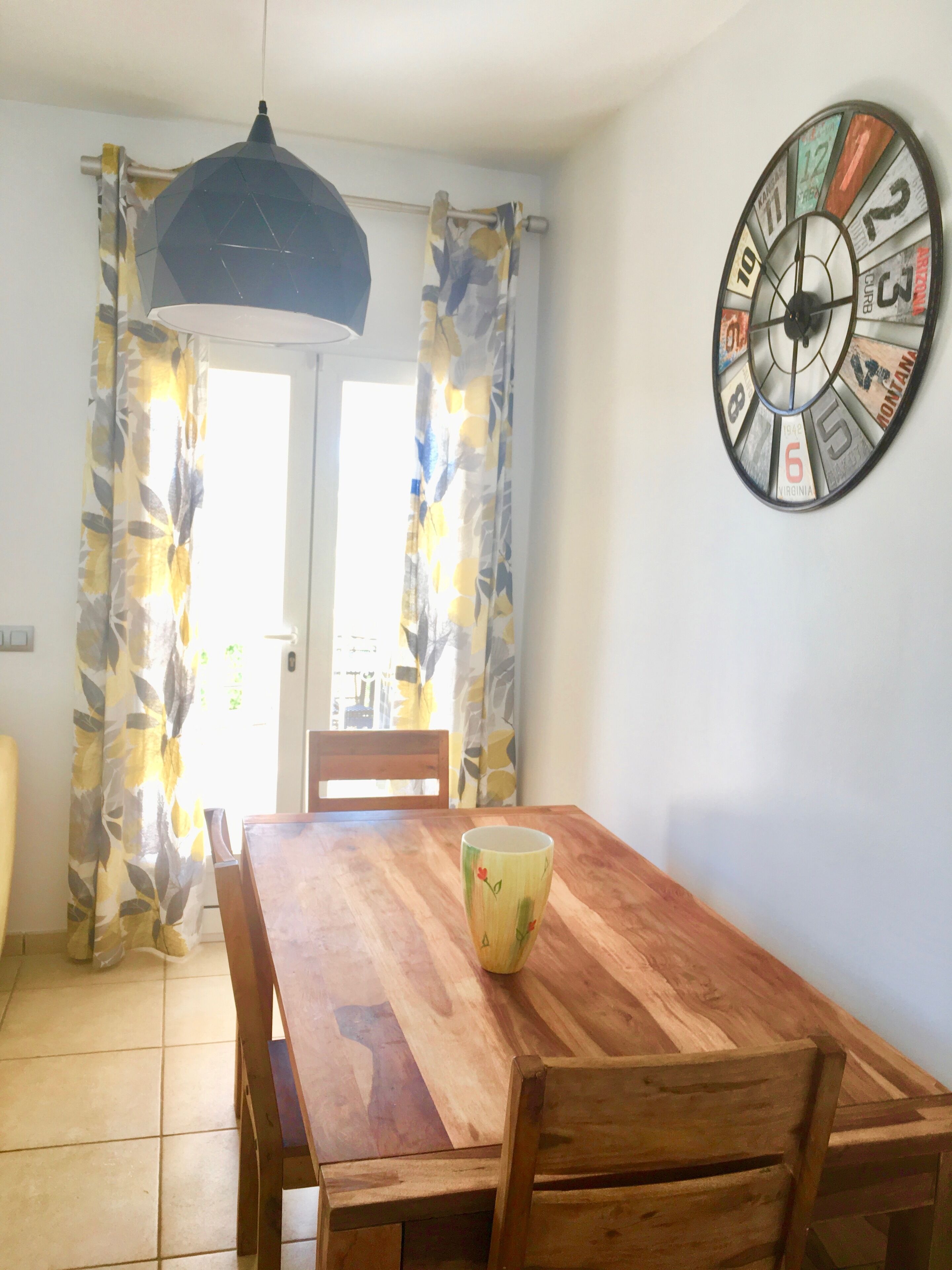 Un coin repas avec une table en bois, des chaises, un vase et une horloge murale.