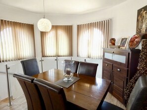 Zona pranzo con tavolo in legno, sedie, un candelabro in vetro e un mobile contenente oggetti decorativi.