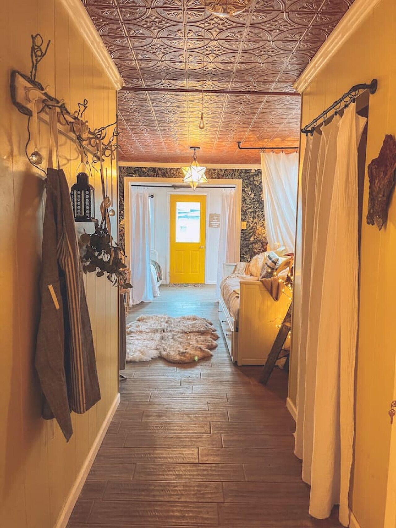 Un estrecho pasillo con pisos de madera, una puerta amarilla al final y un rincón acogedor con una alfombra de piel y cojines.