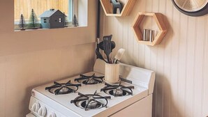 A kitchen with a gas stove, wooden cabinets, and a window with a view of a house and trees. - -Shingle Diggins Cottage- (Coloma)