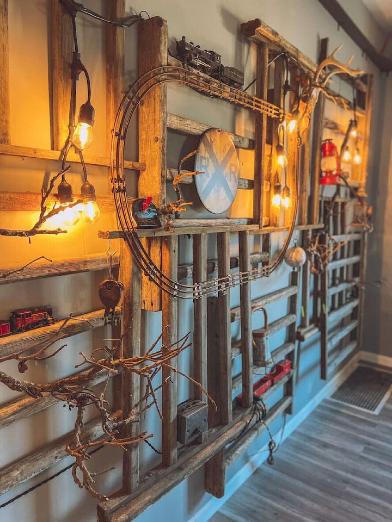 Een muur met een vintage spoorwegthema, inclusief een model treinspoor, een klok en decoratieve elementen zoals takken en lichtjes.