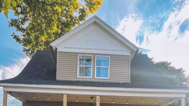 Ein zweistöckiges Haus mit Veranda, einer gelben Tür und einem kleinen Garten.