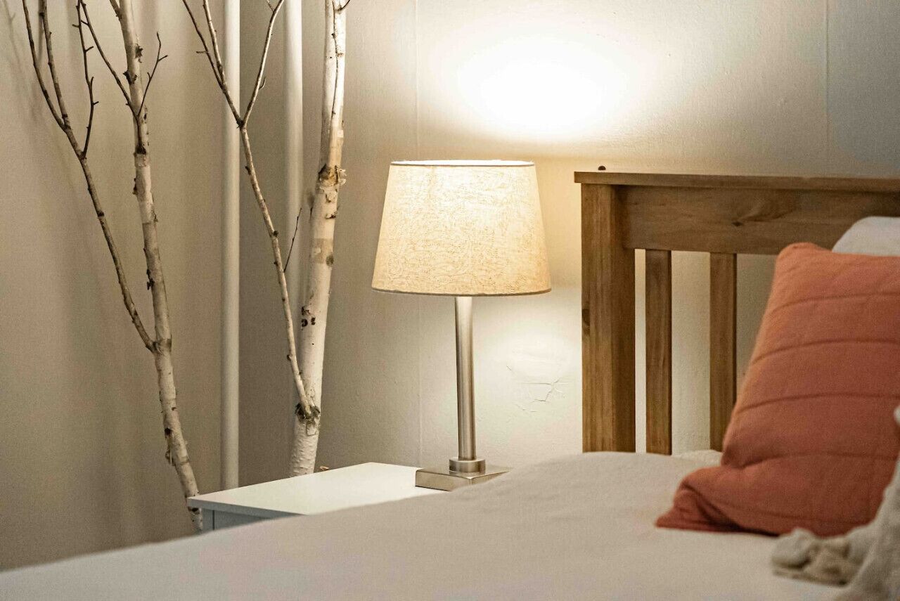 Quarto com cama, mesa de cabeceira, luminária e cabeceira de madeira.