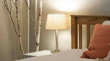Quarto com cama, mesa de cabeceira, luminária e cabeceira de madeira.