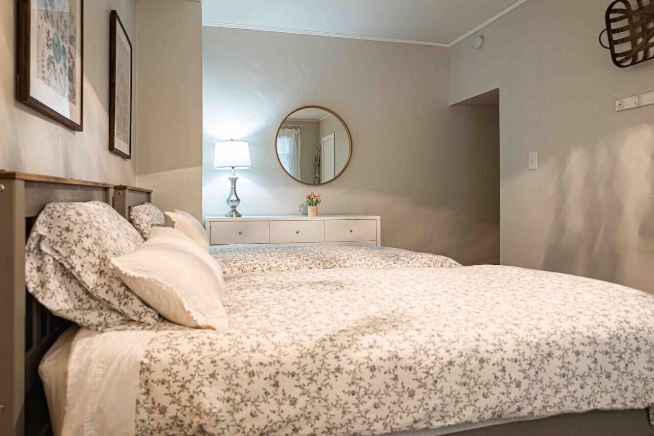 A bedroom with two beds, a dresser, a mirror, and framed pictures on the wall.