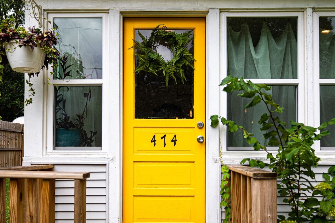 Una puerta amarilla con el número 414, un adorno de flores y plantas colgantes.